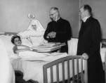 Archbishop Meyer visits Luci Mordini, a survivor of room 208. With Archbishop are Sister H. Alumnda, PHJC, administrator of St. Anne Hospital, and Rev. Richard J. Burmingham, hospital chaplain. (Photo courtesy of The Catholic New World with photo research by Renee Jackson)